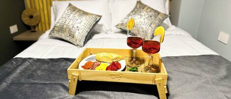 A wooden tray with food and drinks on a bed.