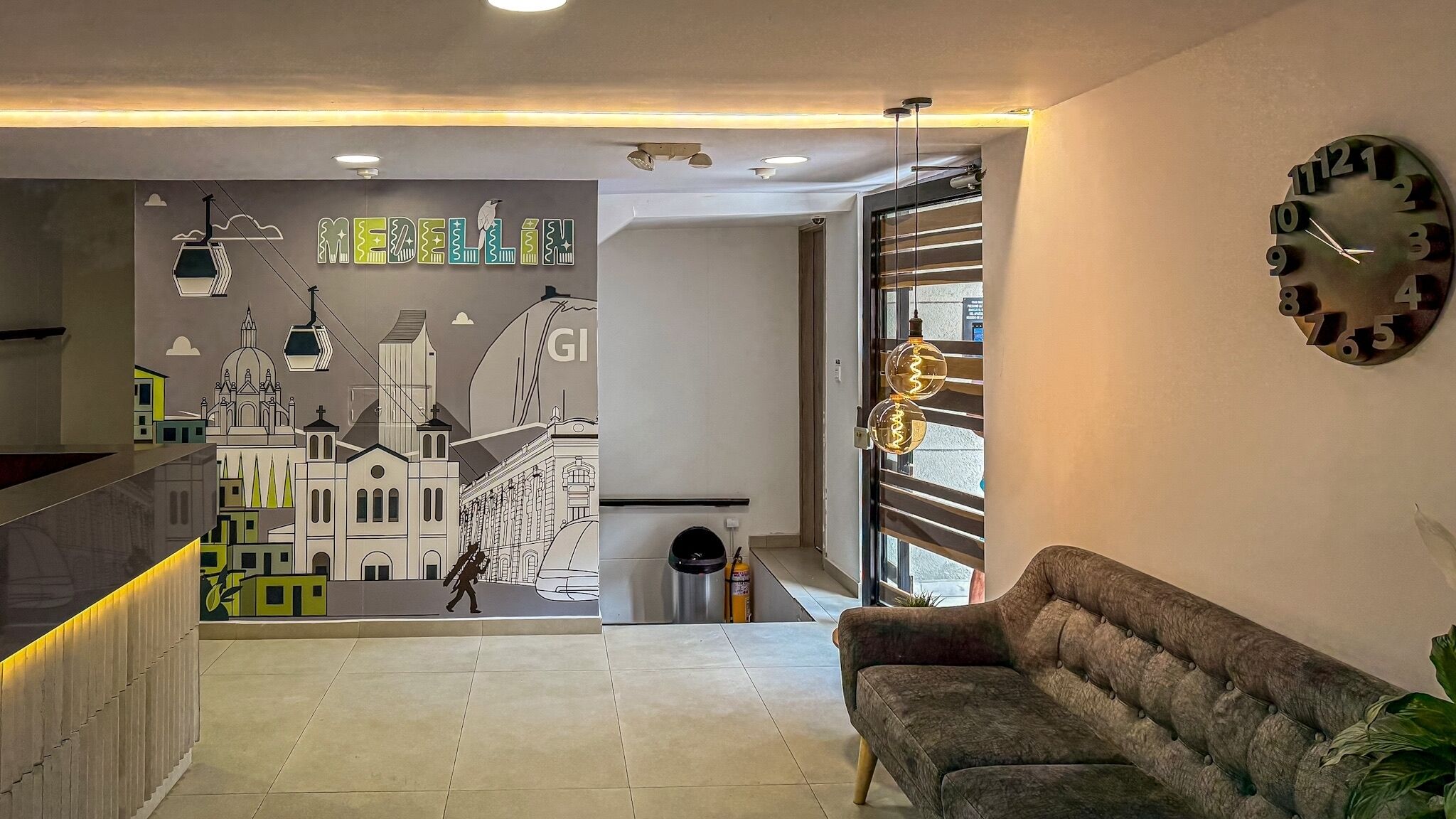 Vestíbulo de hotel con un mural de un paisaje urbano, un sofá y un reloj de pared.