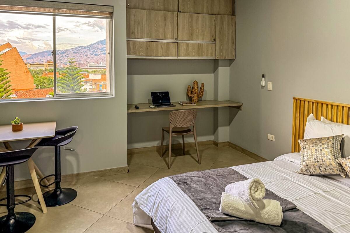 Ein Schlafzimmer mit Bett, Schreibtisch, Stuhl und Fenster mit Blick auf die Stadt.