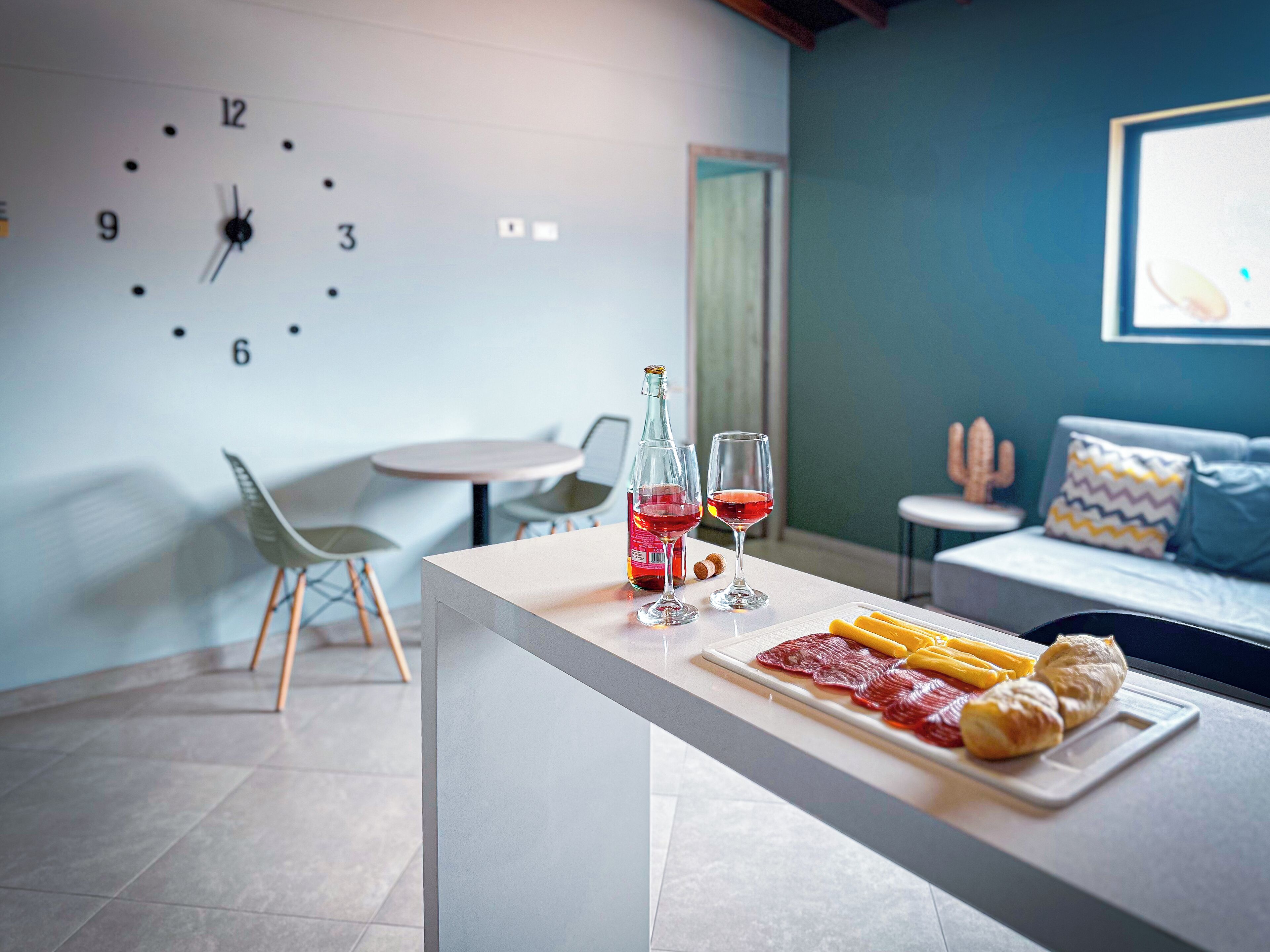 A modern kitchen with a white countertop, a clock on the wall, and a dining area with chairs and a table.