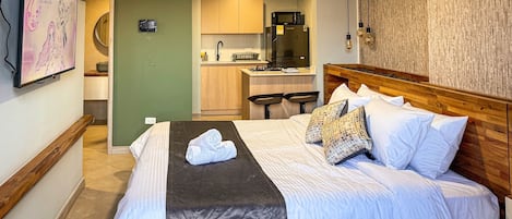 A hotel room with a bed, a small kitchenette, a microwave, and a bar area.