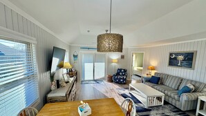 En rummelig stue med et træspisebord, en stribet sofa og en stor hængende lampe.
