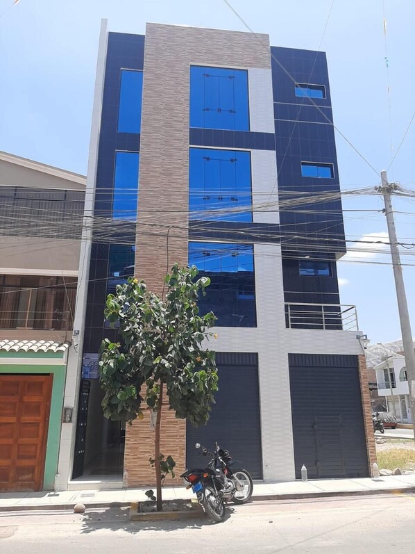 Un edificio moderno de varios pisos con grandes ventanales y un árbol en primer plano.
