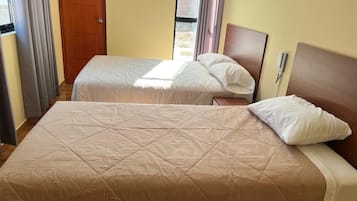 A hotel room with two beds, a wooden door, and a window with curtains.