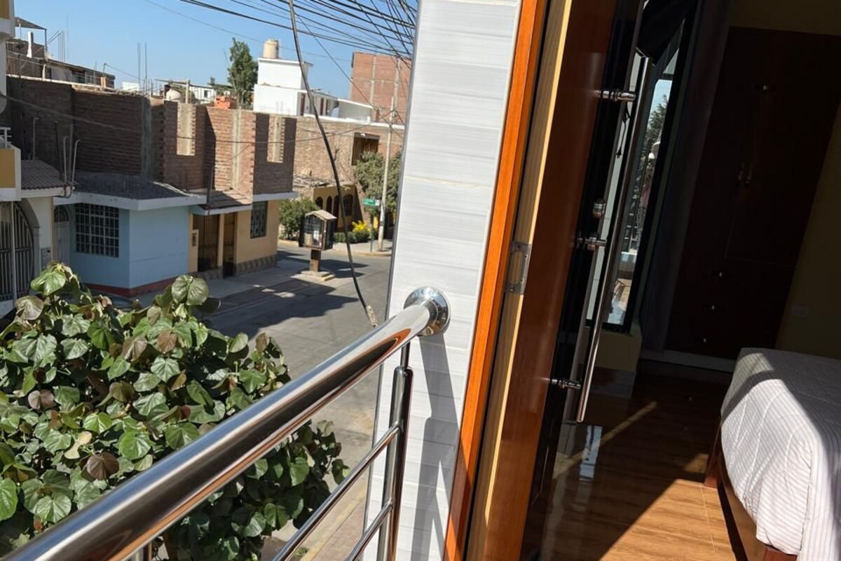 A balcony with a metal railing overlooking a street with buildings and a tree.