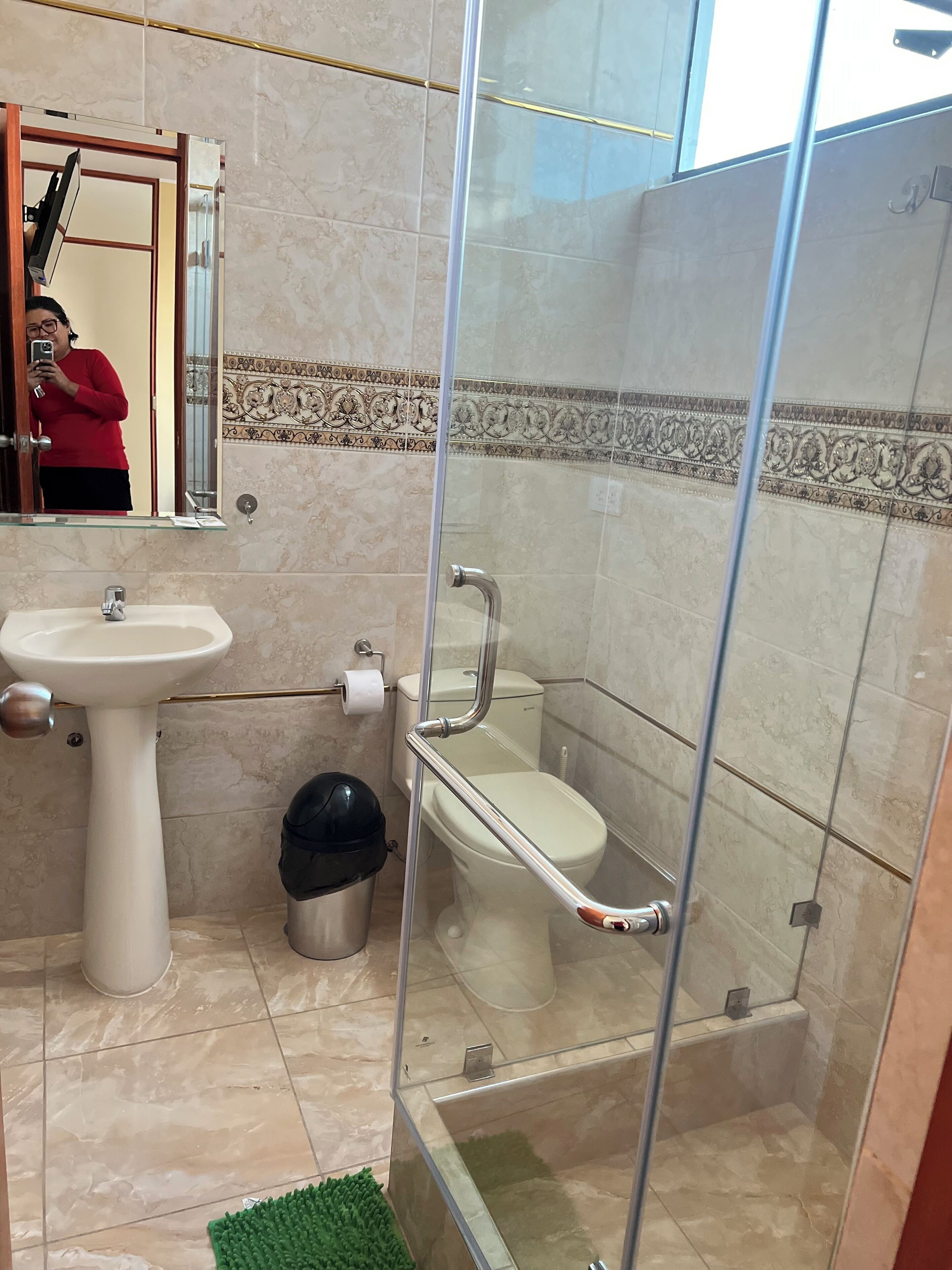 Un baño con cabina de ducha de vidrio, lavamanos pedestal y inodoro.