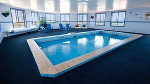 An indoor swimming pool with clear blue water, surrounded by blue chairs and a small table.