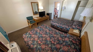 Una habitación de hotel con dos camas, un escritorio con silla, una televisión y un espejo.