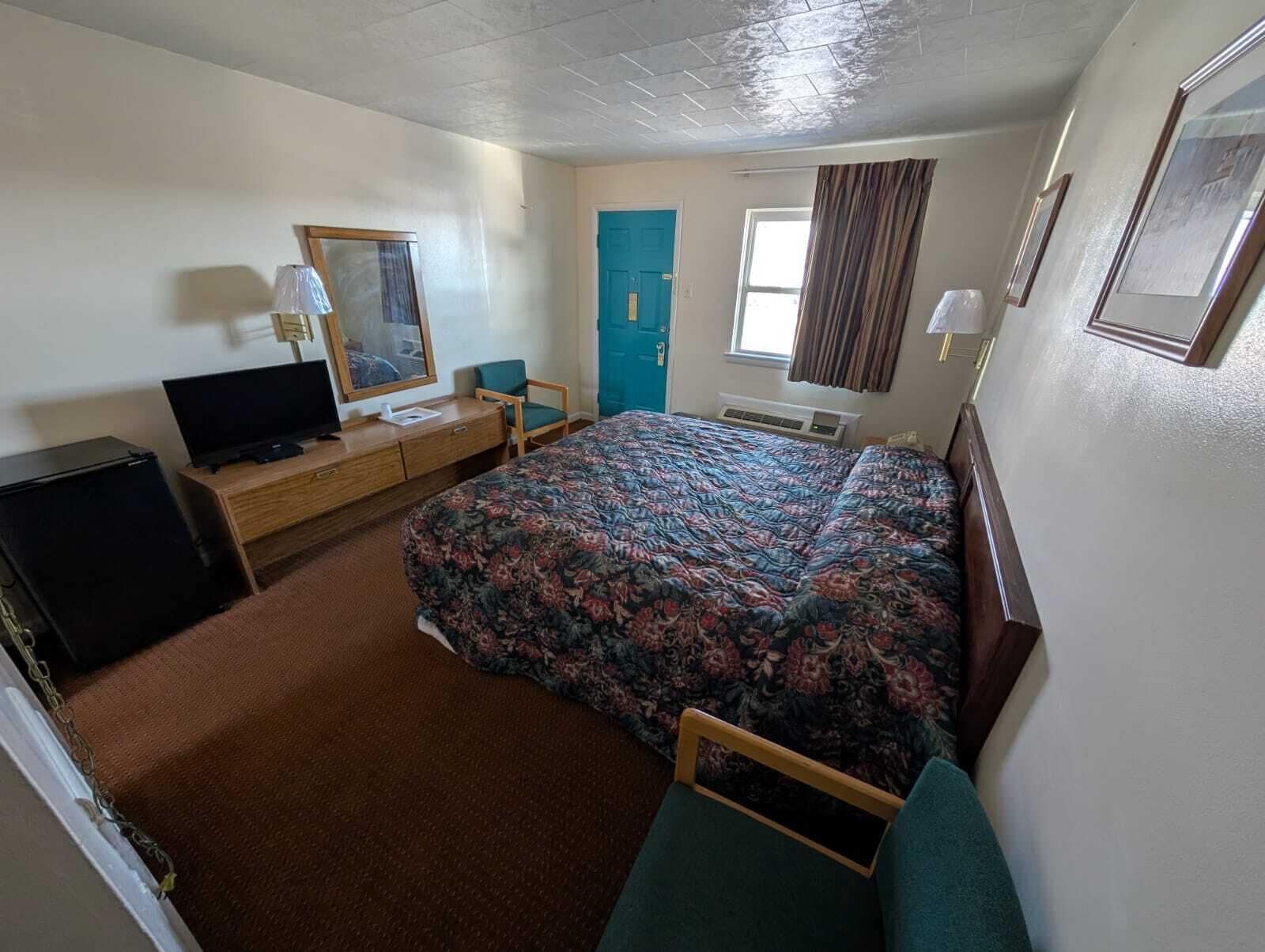 A hotel room with a bed, a television, a desk, a chair, a door, and a window.