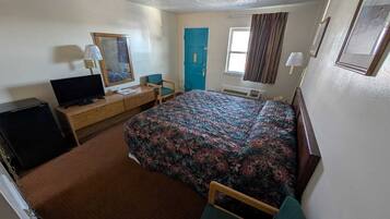 A hotel room with a bed, a television, a desk, a chair, a door, and a window.