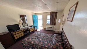 A hotel room with a bed, a desk, a television, a dresser, and a window with curtains. - Relax Inn (New Castle)