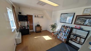 A room with a wooden floor, a radiator, a television on a stand, a small cabinet, a door labeled "PRIVATE," a framed map on the wall, and a magazine rack. - Relax Inn (New Castle)