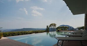 A swimming pool with lounge chairs, a view of mountains, and a clear sky.