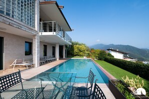 A modern house with a swimming pool, outdoor seating, and a view of mountains.