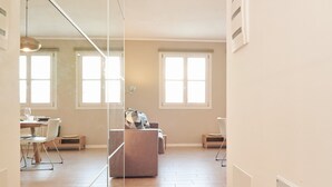 Un vaste espace de vie comprenant un canapé, une table à manger et des chaises. De grandes fenêtres laissent entrer la lumière naturelle.