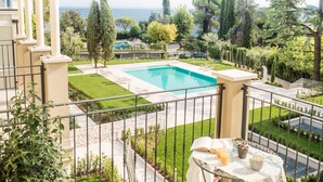 Un espace piscine avec vue sur la mer, entouré de verdure et délimité par une clôture blanche.