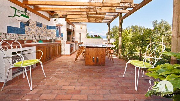 An outdoor kitchen area with a wooden table and chairs, a tiled backsplash, and a pergola structure.
