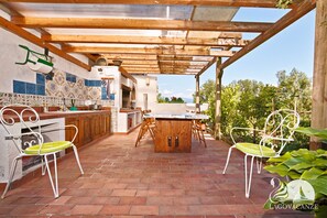 An outdoor kitchen area with a wooden table and chairs, a tiled backsplash, and a pergola structure.