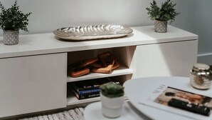 Una mesita de noche blanca con un plato decorativo, una planta pequeña en maceta y un libro.