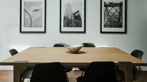 Una sala de conferencias con una mesa de madera, sillas negras y tres fotografías blanco y negro enmarcadas en la pared.
