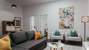 Una sala de estar moderna con un sofá gris, sillones blancos y un cuadro abstracto de colores.