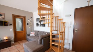 A modern living room with a wooden spiral staircase, a grey sofa, and a wooden door. - Appartamento Francesca (Sirmione)