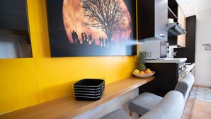 A modern kitchen with a yellow wall, a large painting of silhouetted figures, and a fruit bowl on the counter. - Appartamento Francesca (Sirmione)