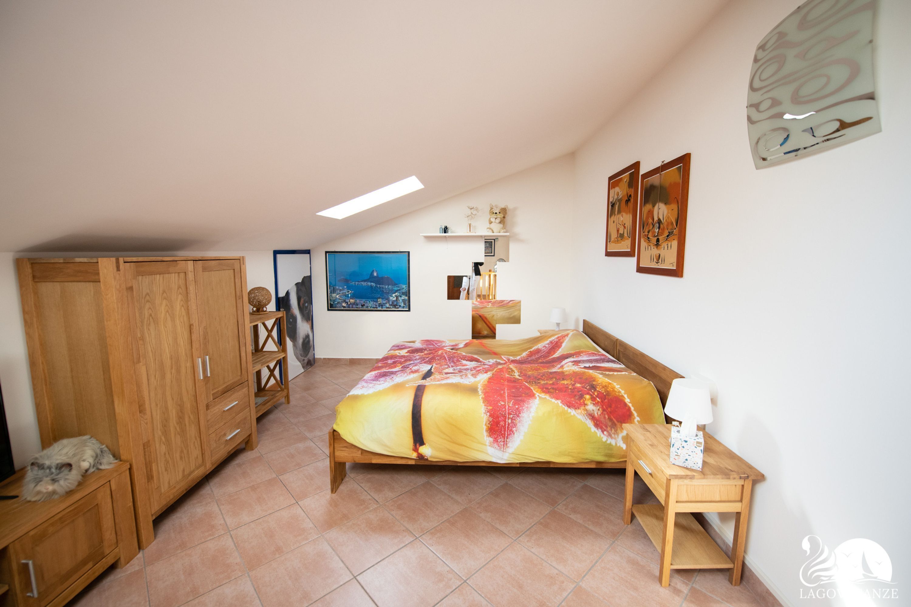 Een slaapkamer met een bed, een houten kledingkast, een nachtkastje, een wandplank en een schilderij.