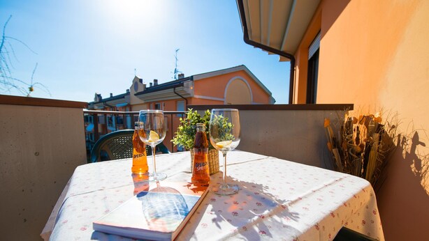 A table with two bottles of Aperol Spritz and two glasses on a balcony with a view of buildings. - Appartamento Francesca (Sirmione)