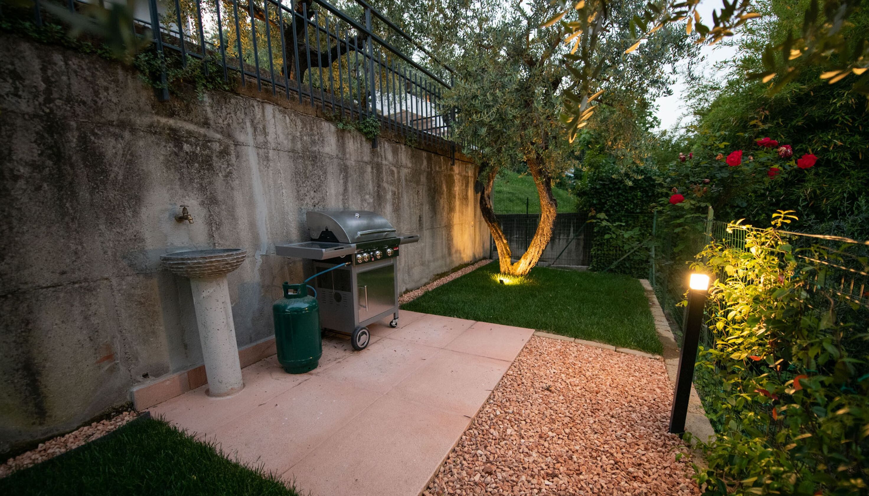 A backyard with a barbecue grill, a gas tank, and a water fountain.