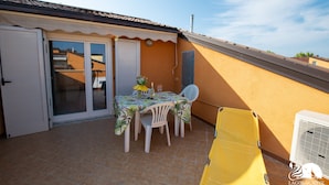Un patio con una mesa y sillas, una silla amarilla, una puerta blanca y un equipo de aire acondicionado blanco.