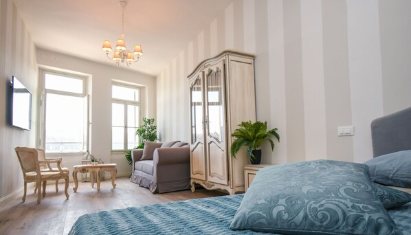A spacious room with a large bed, a wardrobe, a chandelier, a desk, and two chairs.