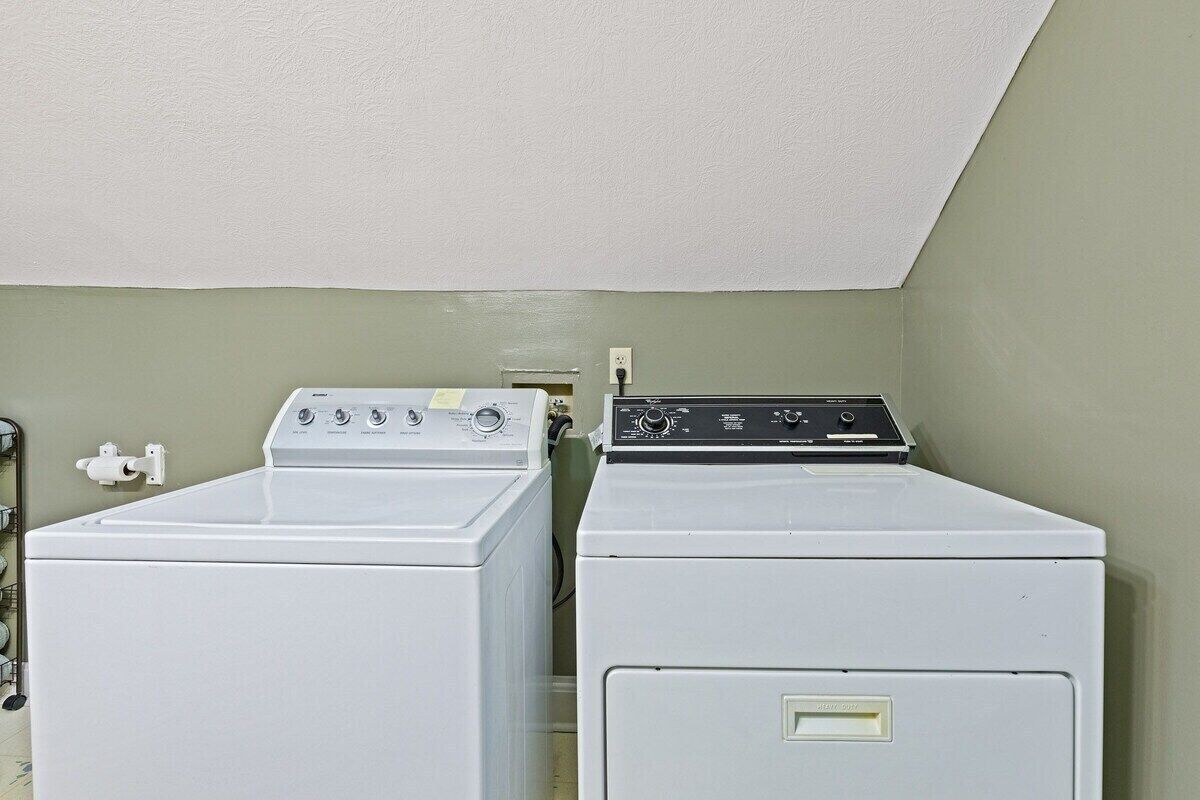 A laundry room with two white washing machines and a dryer, a white ceiling, and a light green wall.