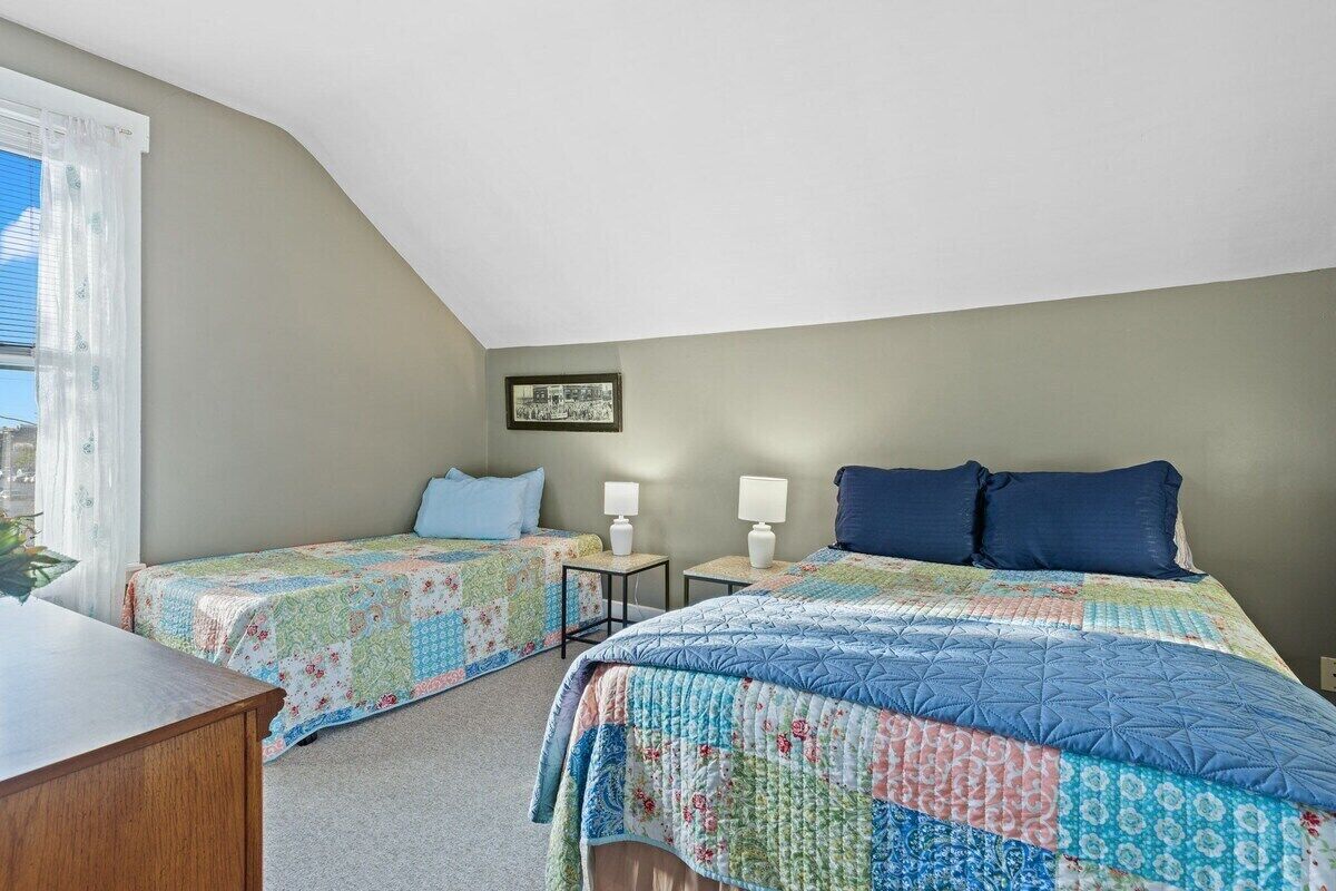 A bedroom with two beds, a desk, and a window with curtains.