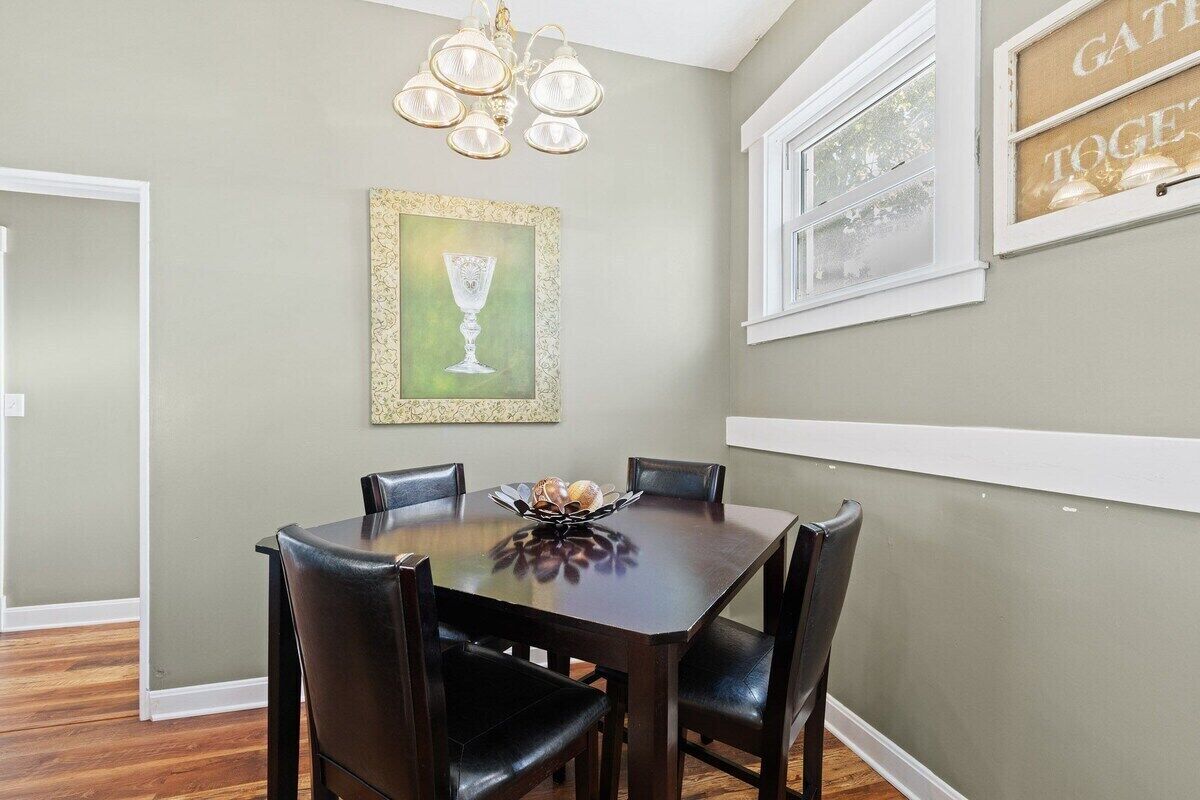 A dining area with a dark wooden table and chairs, a chandelier, and a framed picture on the wall.