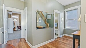 Un couloir doté d’un plancher en bois, d’un escalier et d’une porte donnant sur une autre pièce.