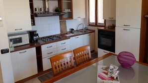 A compact kitchen with white cabinets, a gas stove, a microwave, and a sink. There is a dining table with two chairs and a purple bowl on it. - Casa el Paso in Padenghe sul Garda (Padenghe sul Garda)