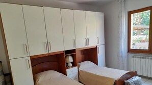 A room with two single beds, a wardrobe, a small table, and a window with a view of greenery. - Casa el Paso in Padenghe sul Garda (Padenghe sul Garda)