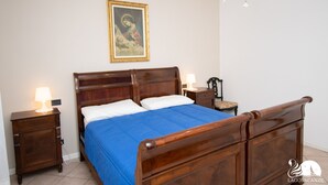 A bedroom with a wooden bed, a nightstand with a lamp, a bedside table, and a framed picture on the wall. - Villa Jole in Polpenazze del Garda (Polpenazze del Garda)
