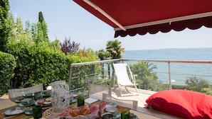 A balcony with a table set for dining, overlooking a body of water and greenery. - Villa Lydia in Padenghe sul Garda (Padenghe sul Garda)