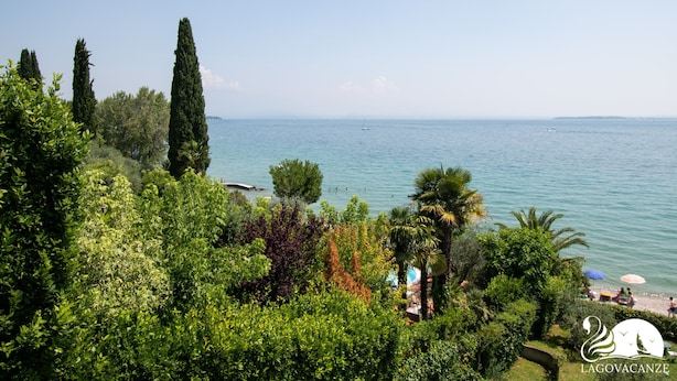 A coastal view with dense greenery, a clear sky, and a distant boat. - Villa Lydia in Padenghe sul Garda (Padenghe sul Garda)