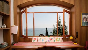 A room with a large window overlooking a body of water, a wooden desk with a lamp, and a shelf with books and decorative items. - Villa Lydia in Padenghe sul Garda (Padenghe sul Garda)