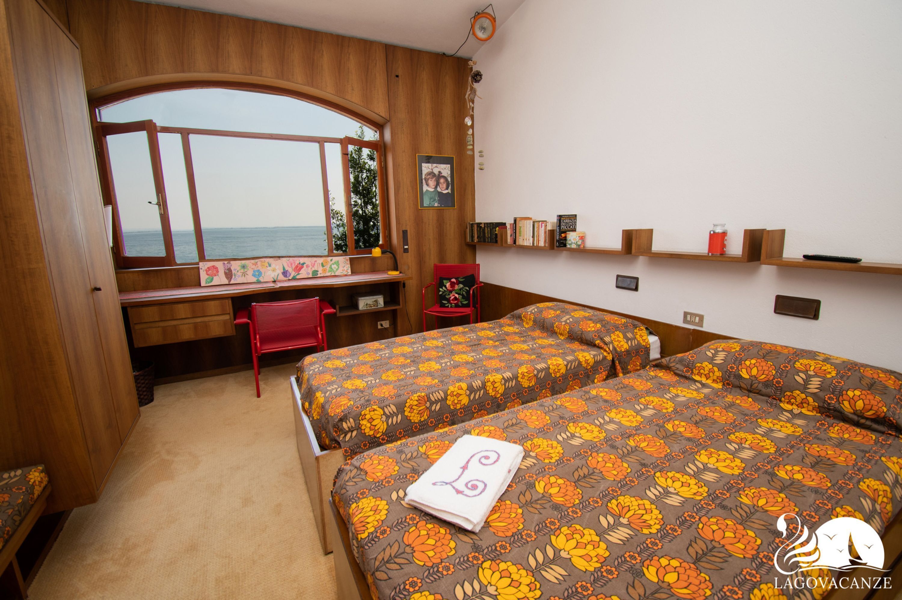 A bedroom with two beds, a desk, a chair, and a window with a view.