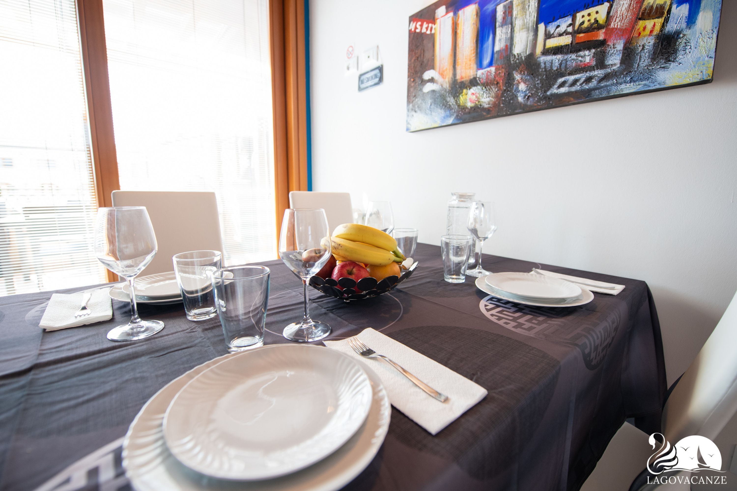 A dining table set with plates, glasses, and a fruit bowl.