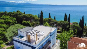 A modern building with a rooftop terrace overlooking a body of water, surrounded by greenery. - Soleblu Appartamento 03 (Padenghe sul Garda)