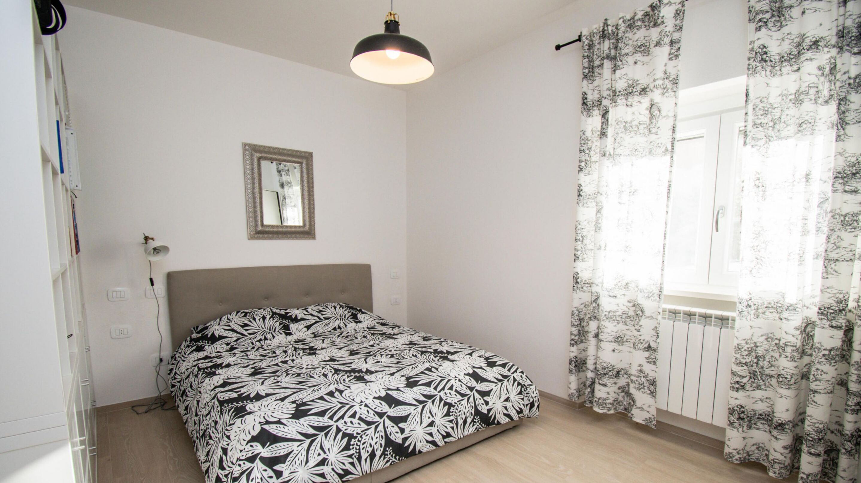 A bedroom with a bed, a ceiling light, a mirror, and a window with curtains.