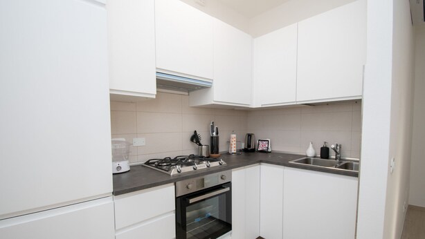 A modern kitchen with white cabinets, a gas stove, a built-in oven, and a stainless steel sink. - Soleblu Appartamento 03 (Padenghe sul Garda)