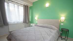 Un dormitorio con cama, mesita de noche, lámpara y radiador.