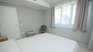 A bedroom with a bed, a chair, a window with curtains, and a door. - Luxury Martina Appartamenti-2-ortensia (Moniga del Garda)
