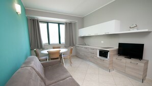 A modern kitchen with a built-in oven, a dining area with a round table and chairs, and a flat-screen TV on a cabinet. - Luxury Martina Appartamenti-2-ortensia (Moniga del Garda)
